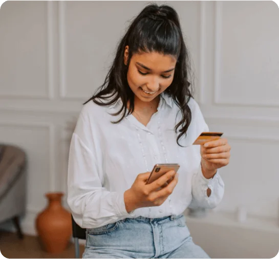 A woman holding a bank card and a smartphone, ready for secure mobile banking or online transactions.