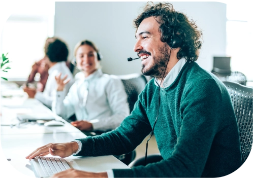 A smiling man having a phone conversation with a customer, with a supportive colleague in the background, providing professional customer service and real-time support.